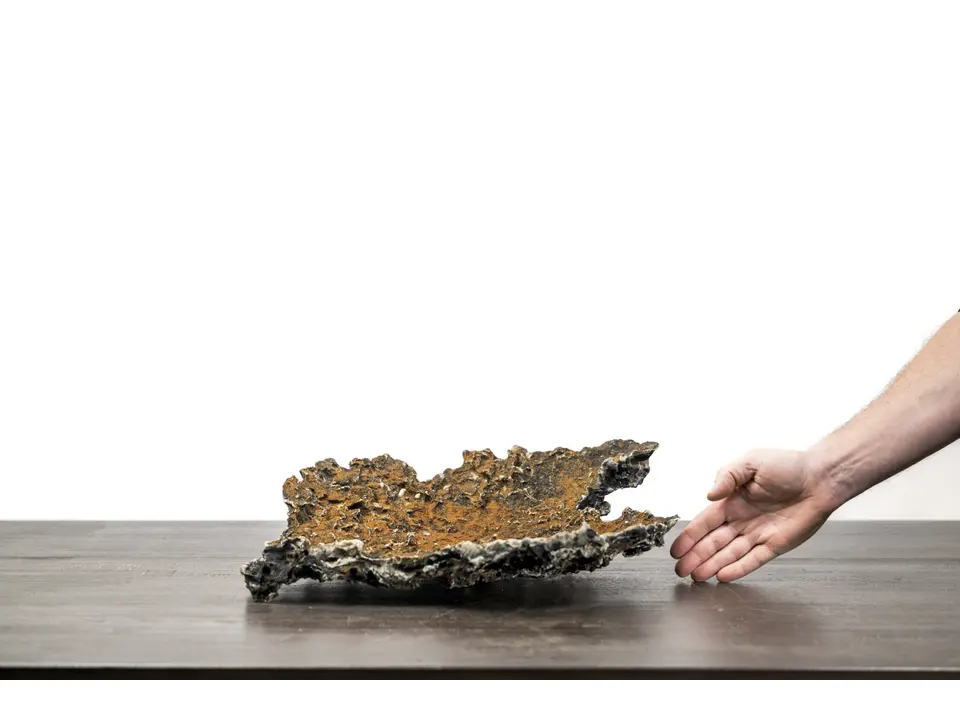 Slab No. 58 rock creation with a hand for scale on a white studio surface