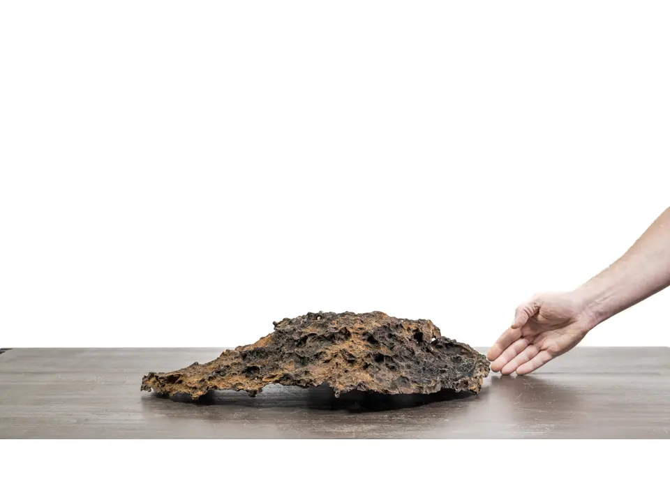 Slab No. 60 rock creation with a hand for scale on a white studio surface